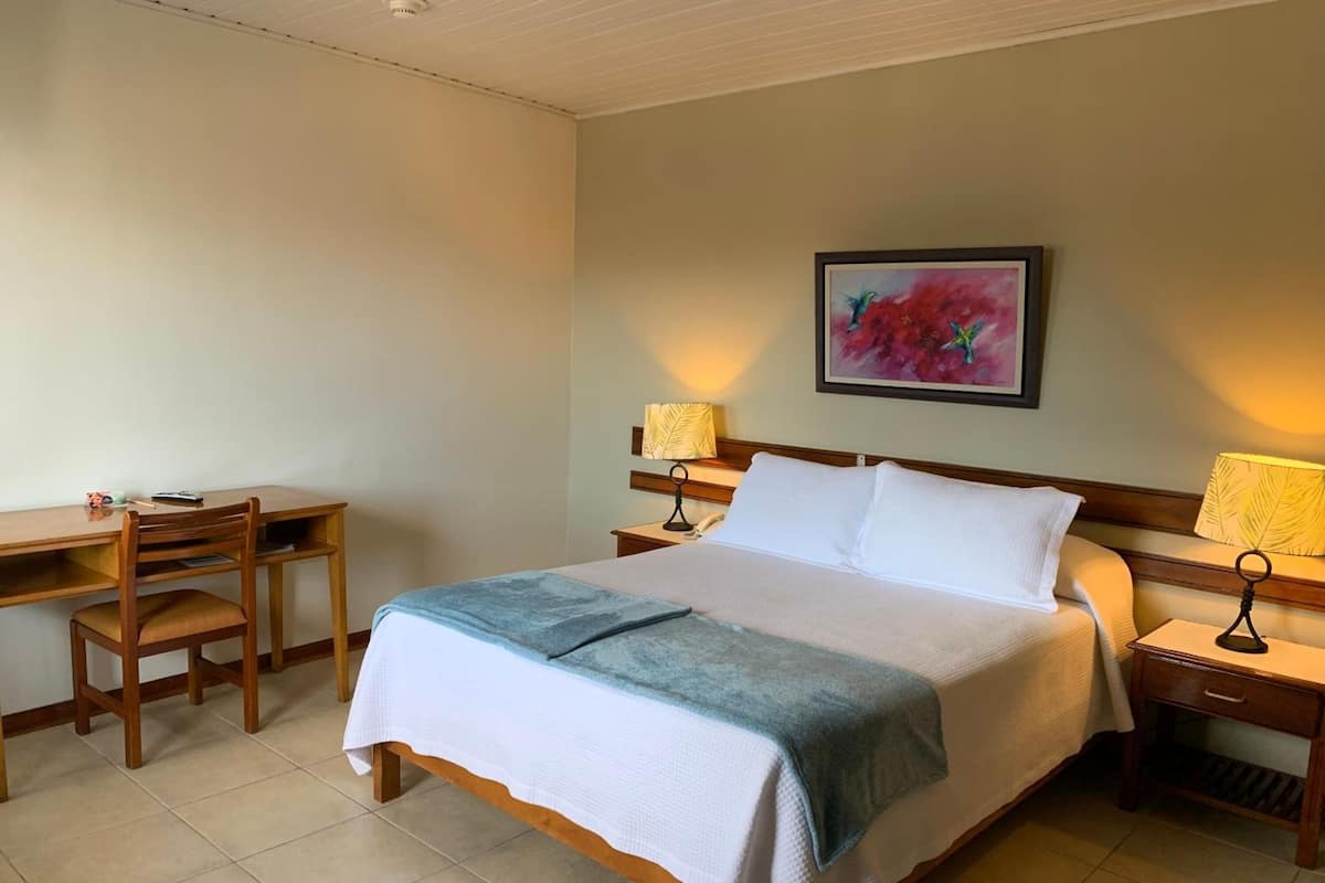 Une chambre d’hôtel comprenant un lit, un bureau, une chaise et deux lampes de chevet.