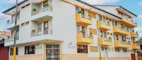 A multi-story hotel with balconies, potted plants, and a visible entrance.