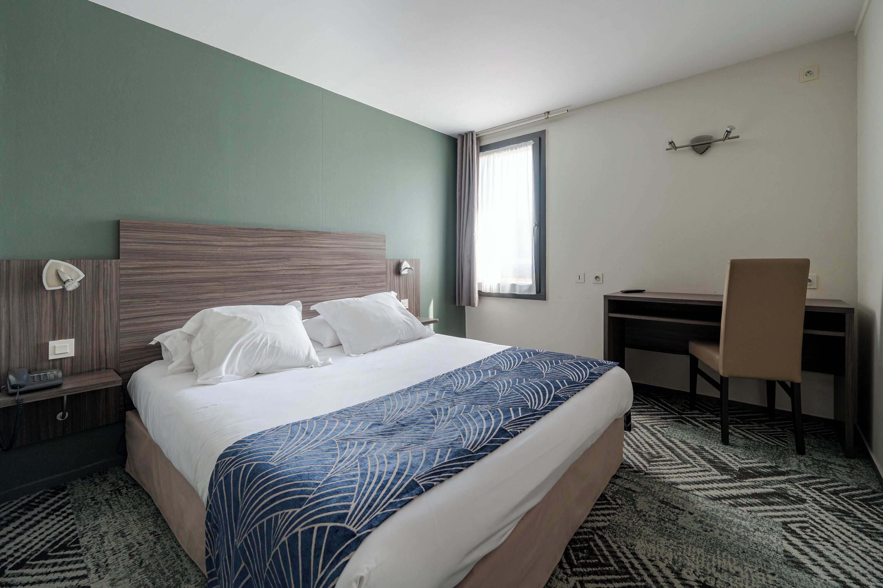 Une chambre d’hôtel équipée d’un lit, d’un bureau, d’une chaise et d’un téléphone posé sur la table de chevet.