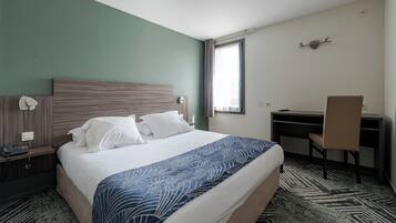 Une chambre d’hôtel équipée d’un lit, d’un bureau, d’une chaise et d’un téléphone posé sur la table de chevet.