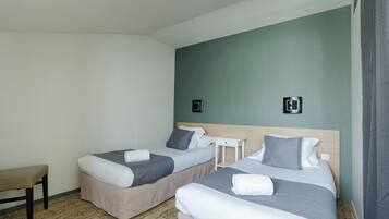Una habitación de hotel con dos camas, una mesita y un banco.
