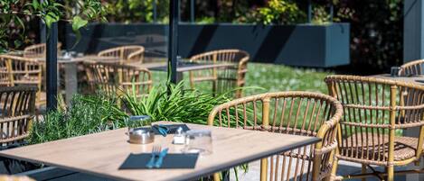 An outdoor dining area with wicker chairs and tables, surrounded by greenery.