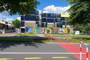 Un immeuble à plusieurs étages doté d’une architecture moderne, orné d’une fresque sur sa façade et bordé d’une piste cyclable rouge.