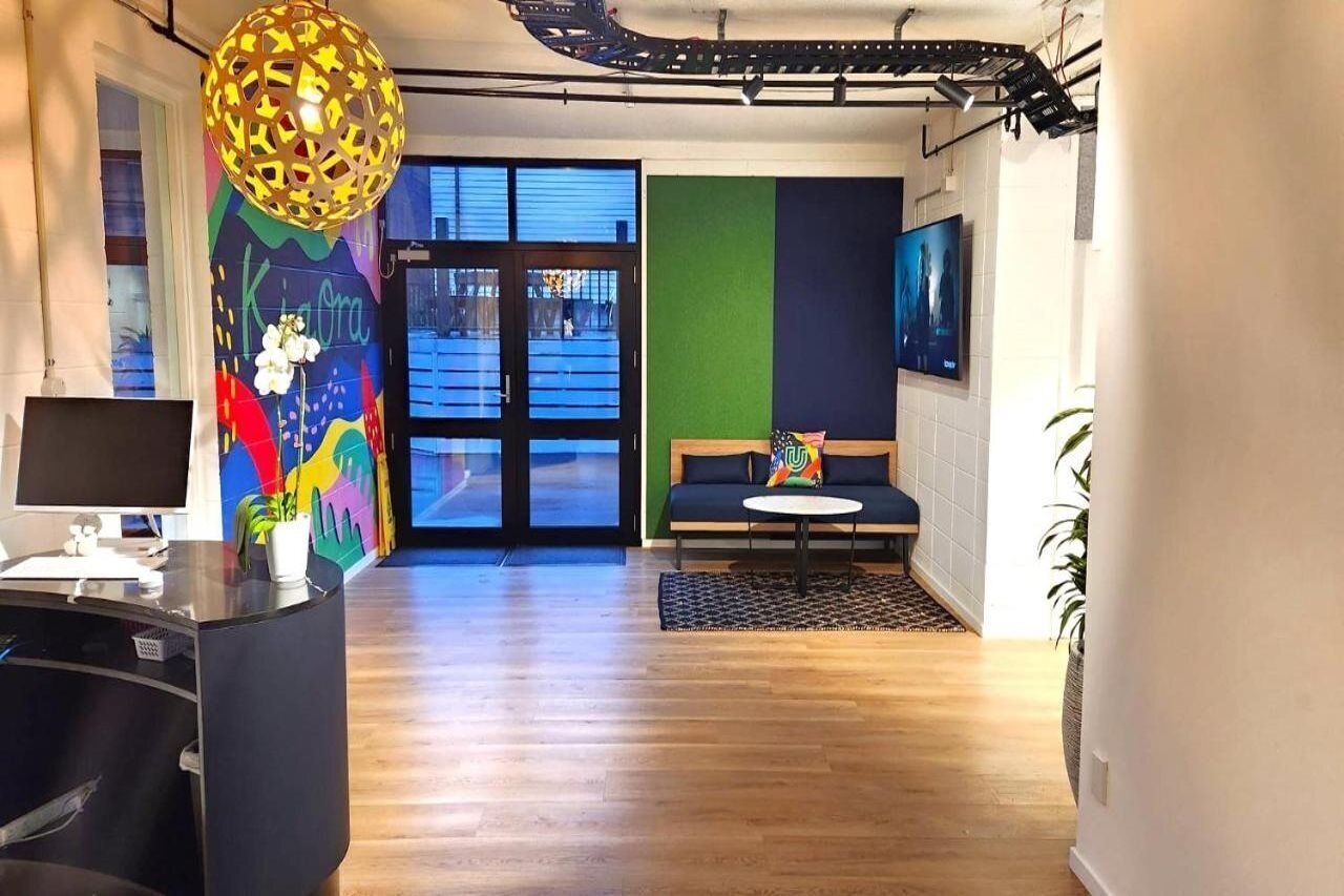 A modern interior with a reception desk, a colorful mural, a sofa, and a large window.