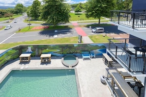 En swimmingpool med solstolar och utsikt över en väg och grönområden.