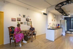 A room with a dining table, chairs, a kitchen area, and a staircase. - Base Rotorua - Hostel (Rotorua)