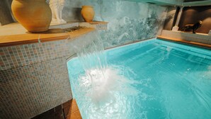 Una piscina con fuente, pared de mosaicos y esculturas clásicas.
