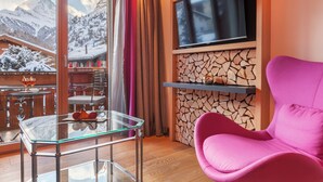Una habitación moderna con una mesa de vidrio, una silla rosa, un televisor montado en una pared de piedra y vistas a montañas nevadas.