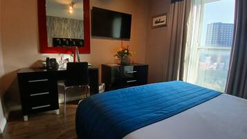 A hotel room with a bed, a desk with a telephone, a television, and a window with curtains.
