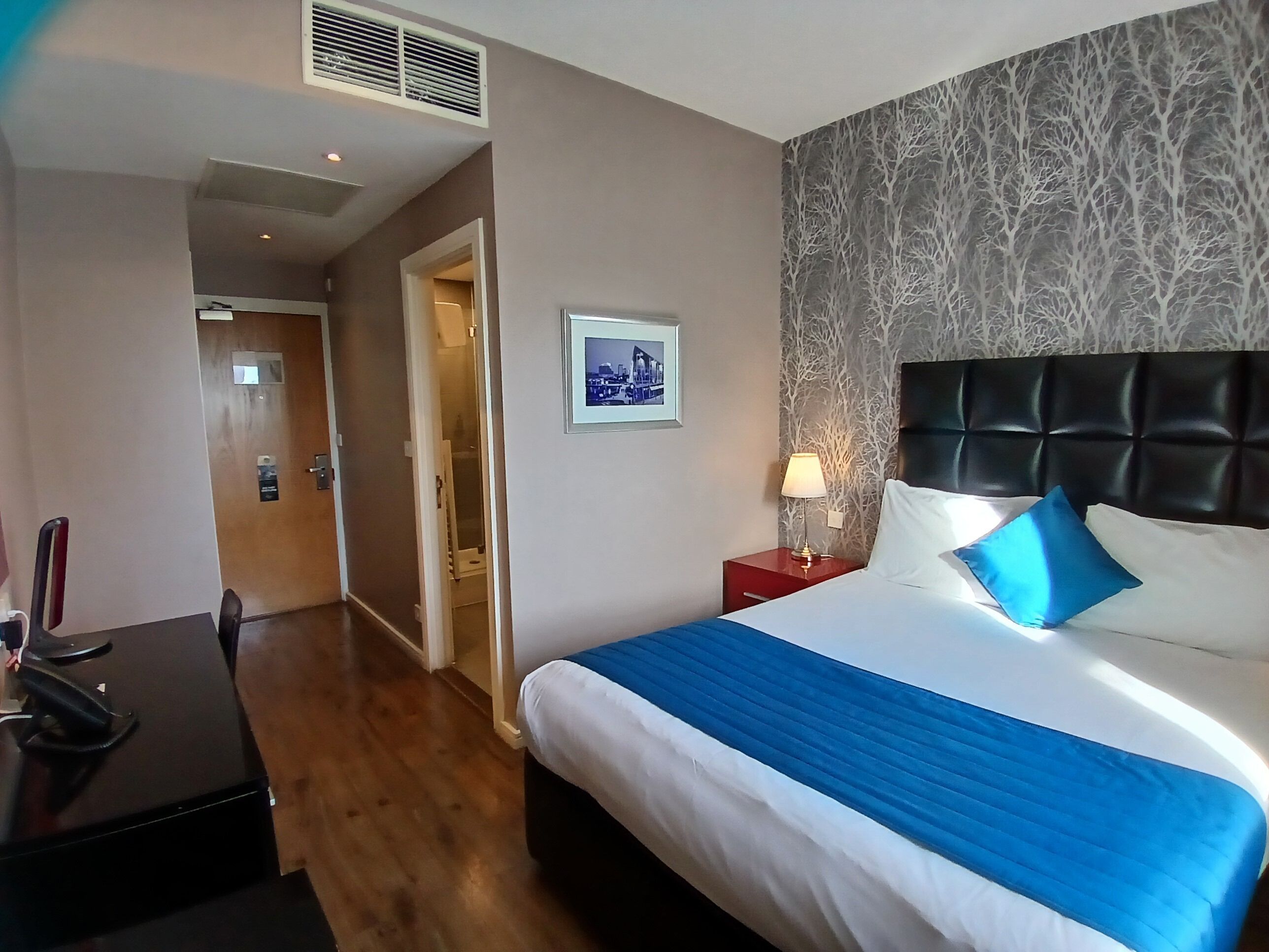A hotel room with a bed, a desk, and a nightstand.