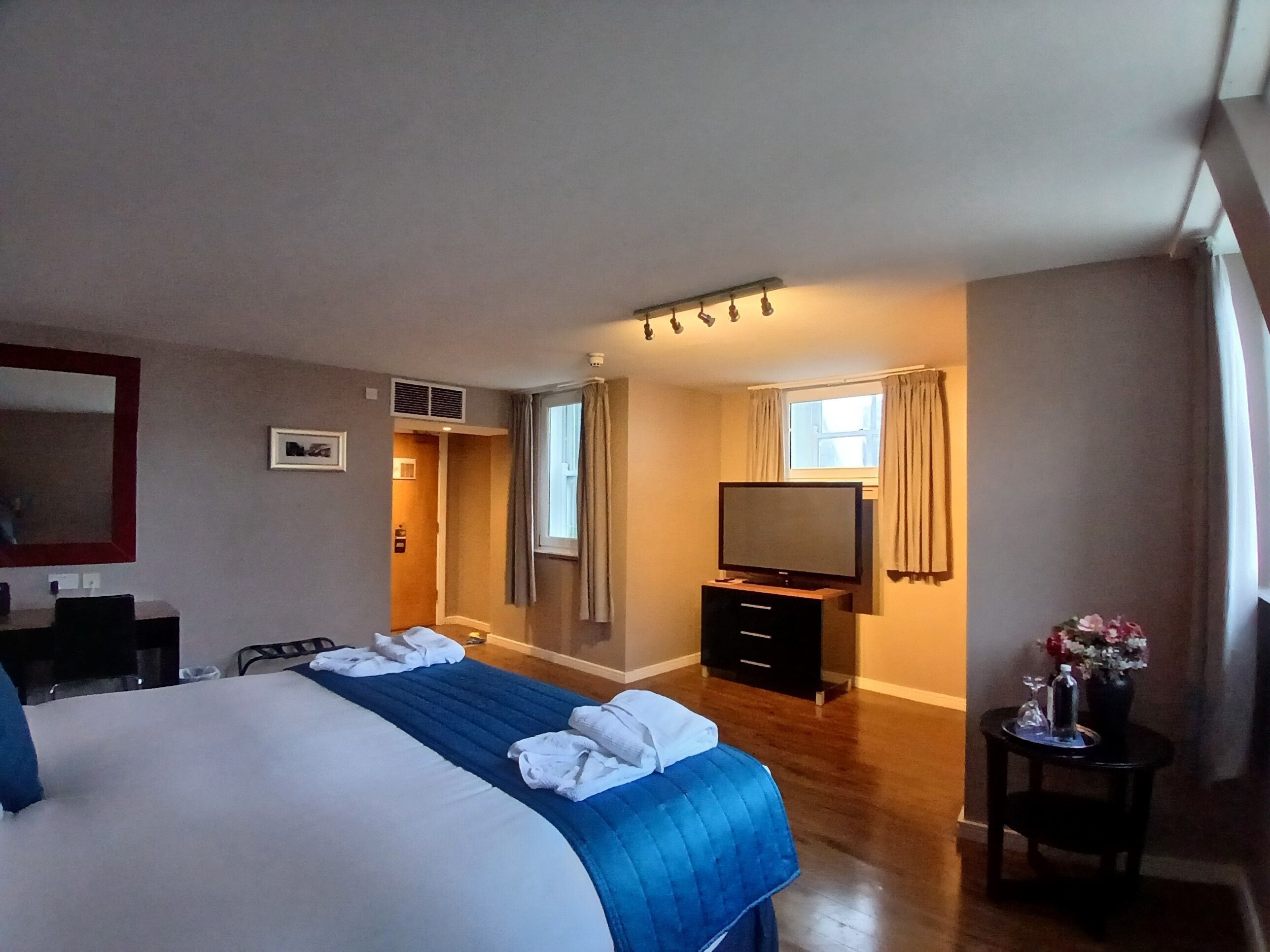 Quarto de hotel com cama grande, televisão, escrivaninha e mesinha com um vaso.