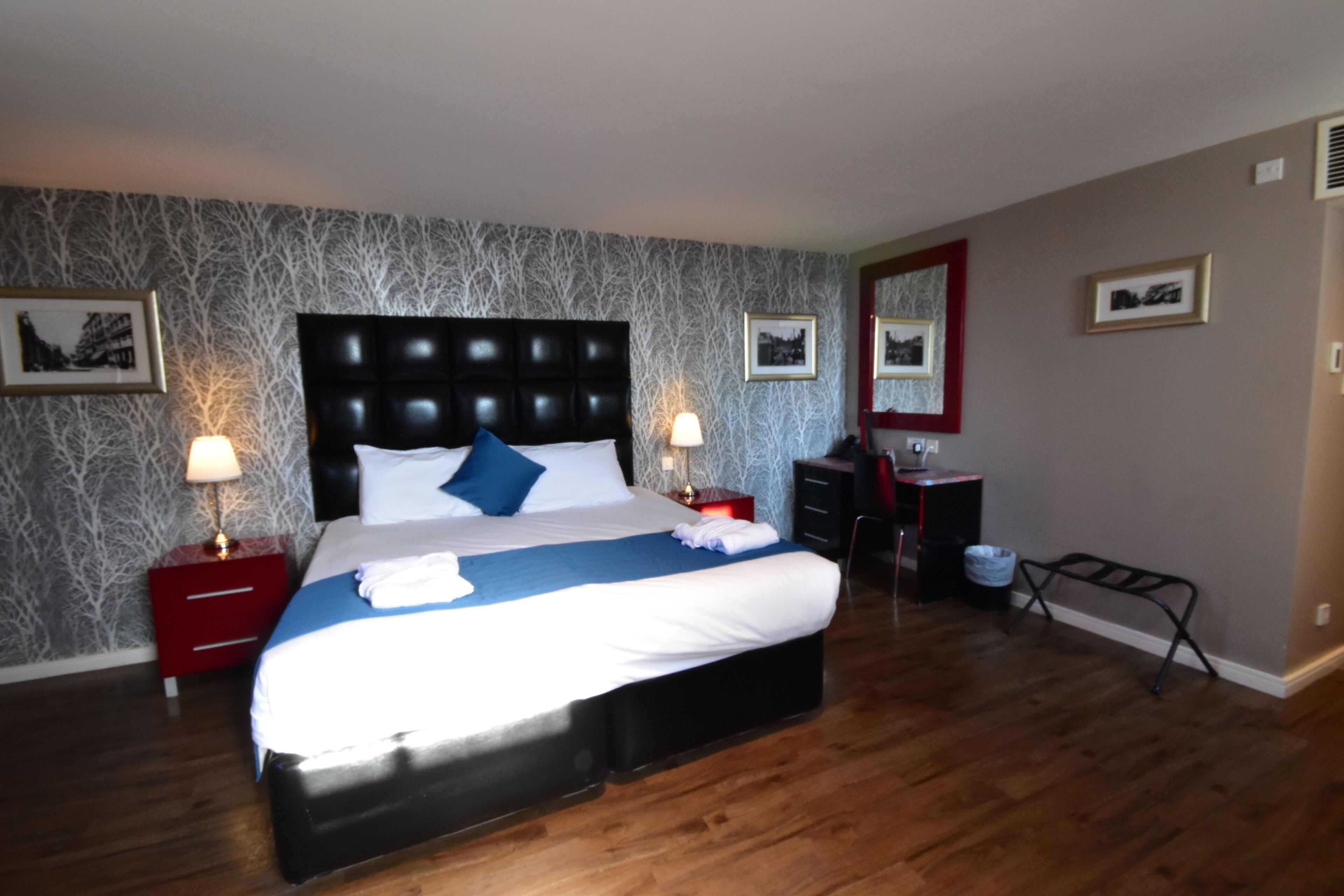 Ein Hotelzimmer mit einem großen Bett, zwei Nachttischen mit Lampen, einer Kommode und einem Spiegel an der Wand.