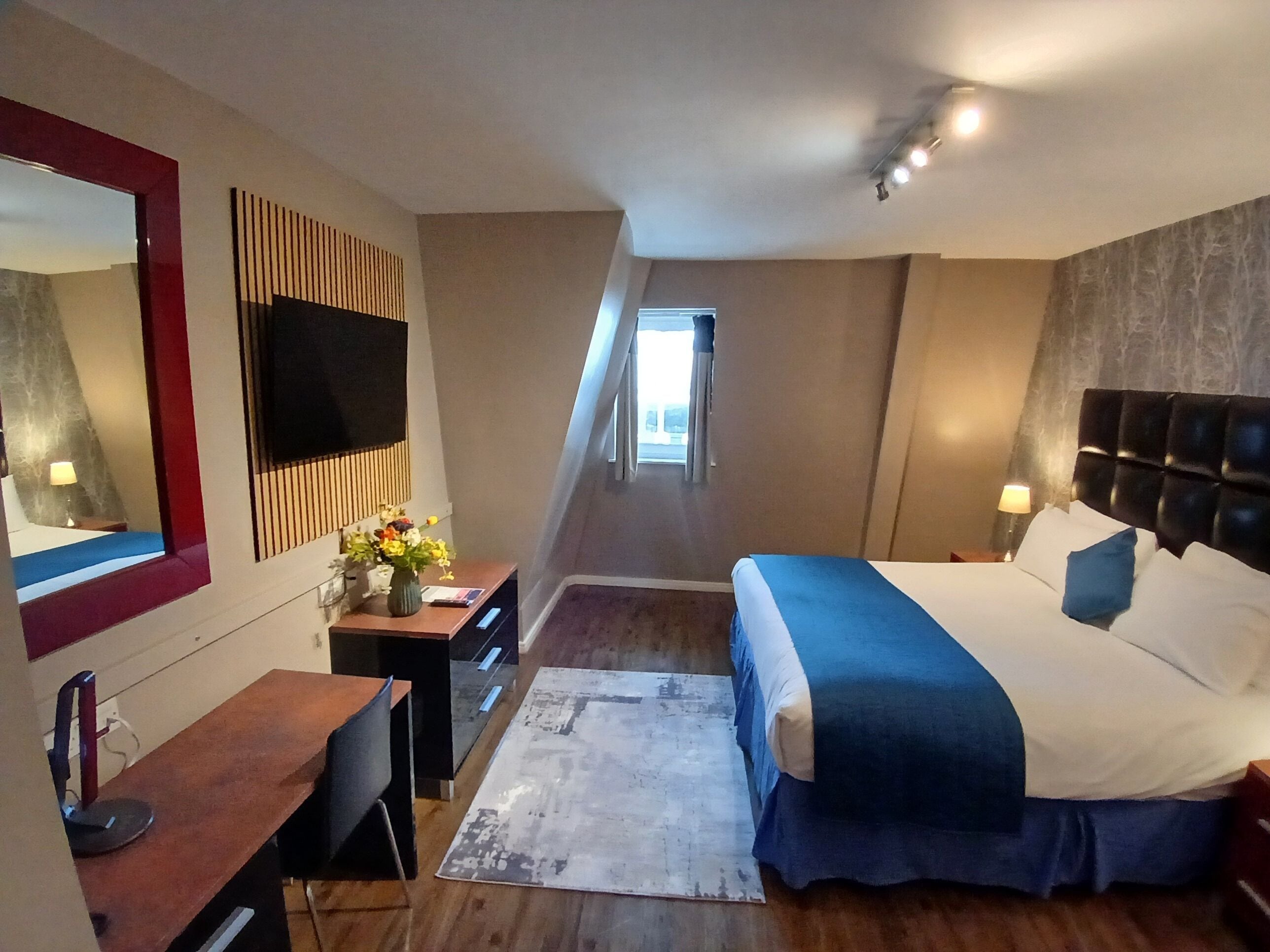 Une chambre d’hôtel avec un lit, un bureau, une chaise et un grand miroir.