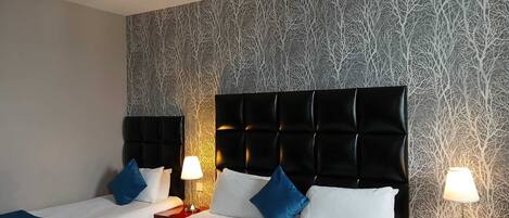 A hotel room with two beds, each with a black headboard, white bedding, and blue accents. There are two bedside tables with lamps.