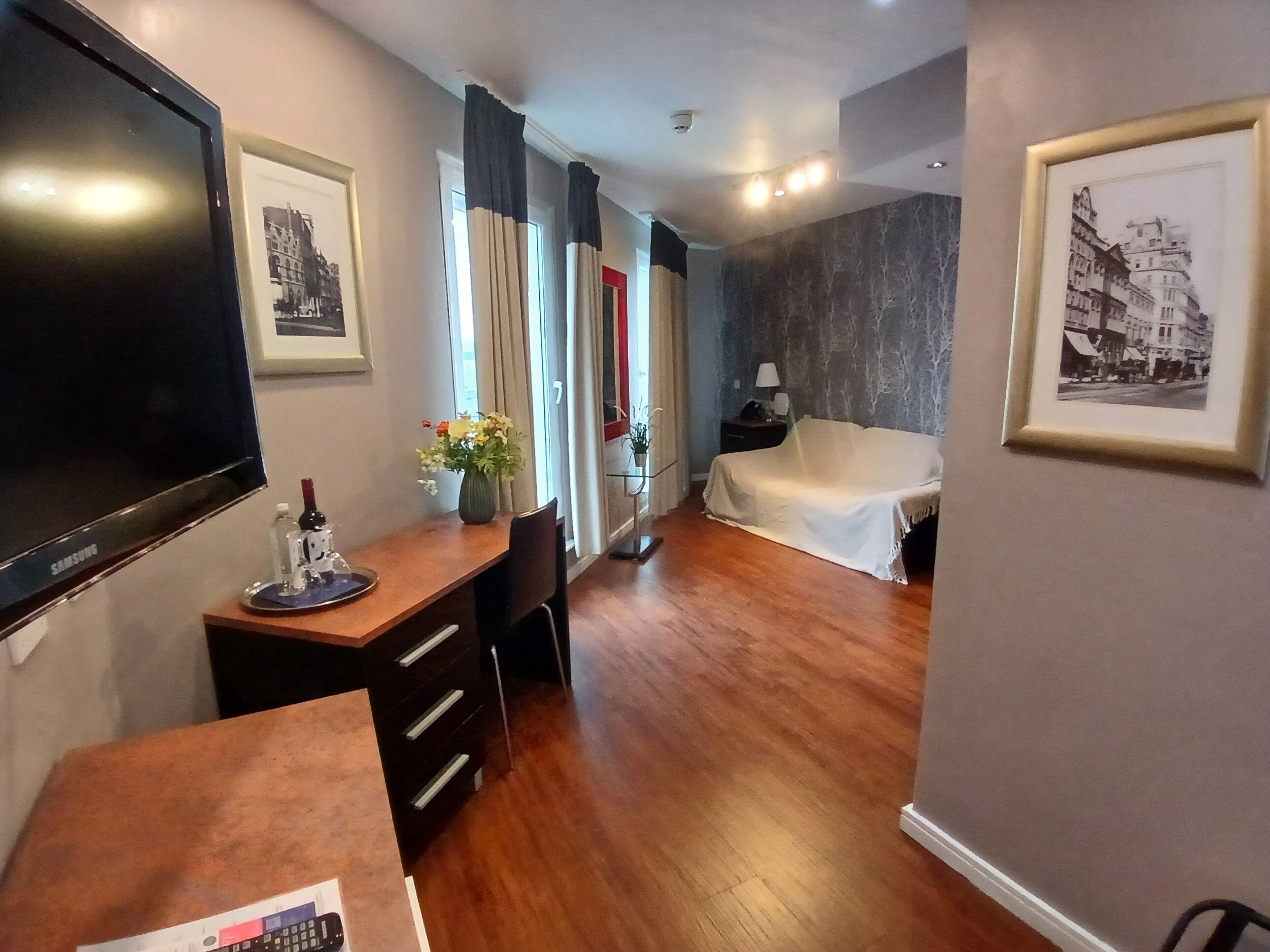 Een hotelkamer met een bed, een bureau met stoel, een televisie en ingelijste foto's aan de muren.