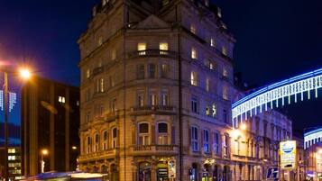 A historic building with classical architecture, a street with a bus, and a brightly lit sign.