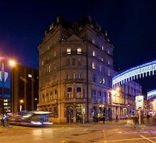 Un edificio histórico con arquitectura clásica, una calle con un autobús y un letrero muy iluminado.