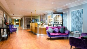 A hotel lobby with a reception desk, purple sofas, a wooden floor, and a patterned wall. - Royal Hotel Cardiff by Belvilla (Cardiff)