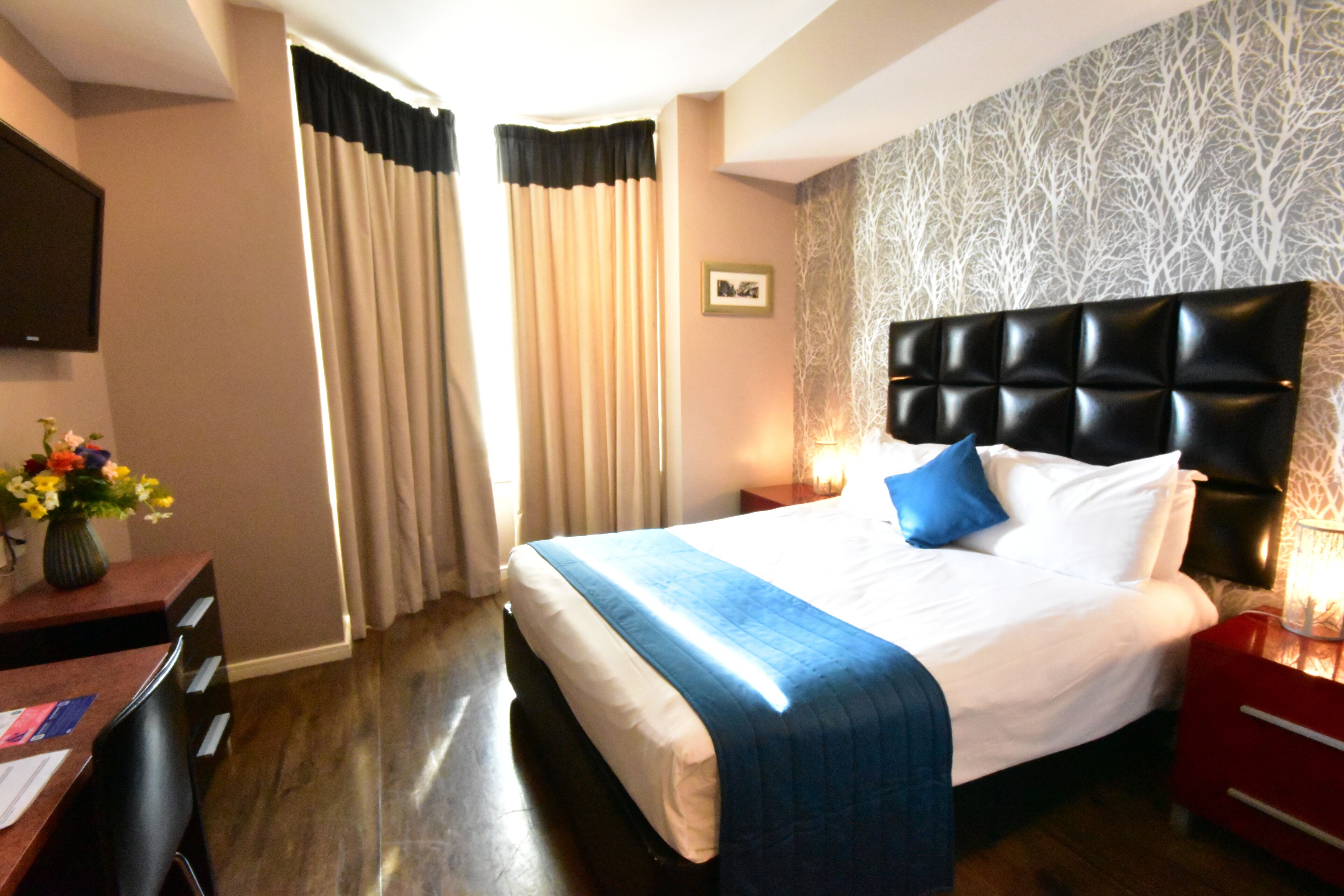 Une chambre d’hôtel avec un grand lit, un bureau avec une chaise, une table de chevet rouge et un téléviseur fixé au mur.