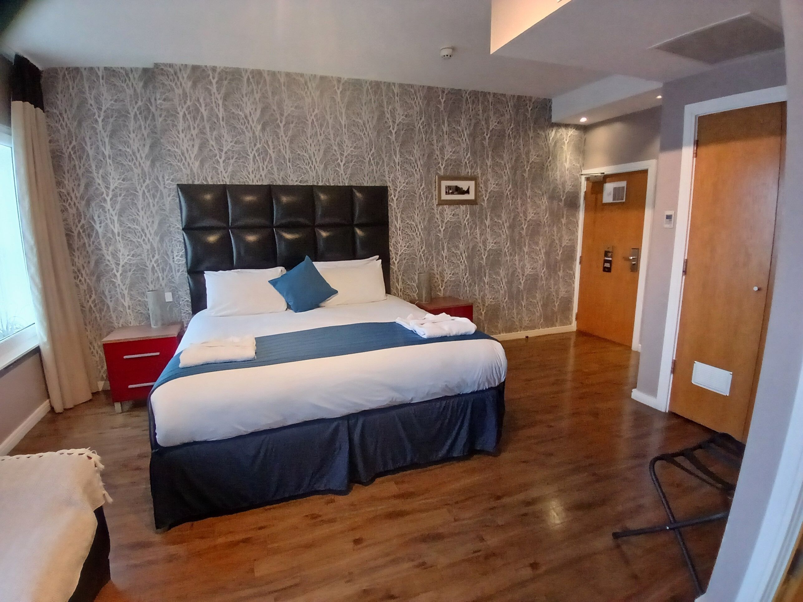 A neatly made bed with a dark headboard, a red nightstand, and a wooden floor.