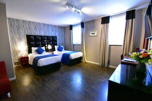 Habitación de hotel con dos camas, un escritorio, una silla, un televisor y una ventana con cortinas.
