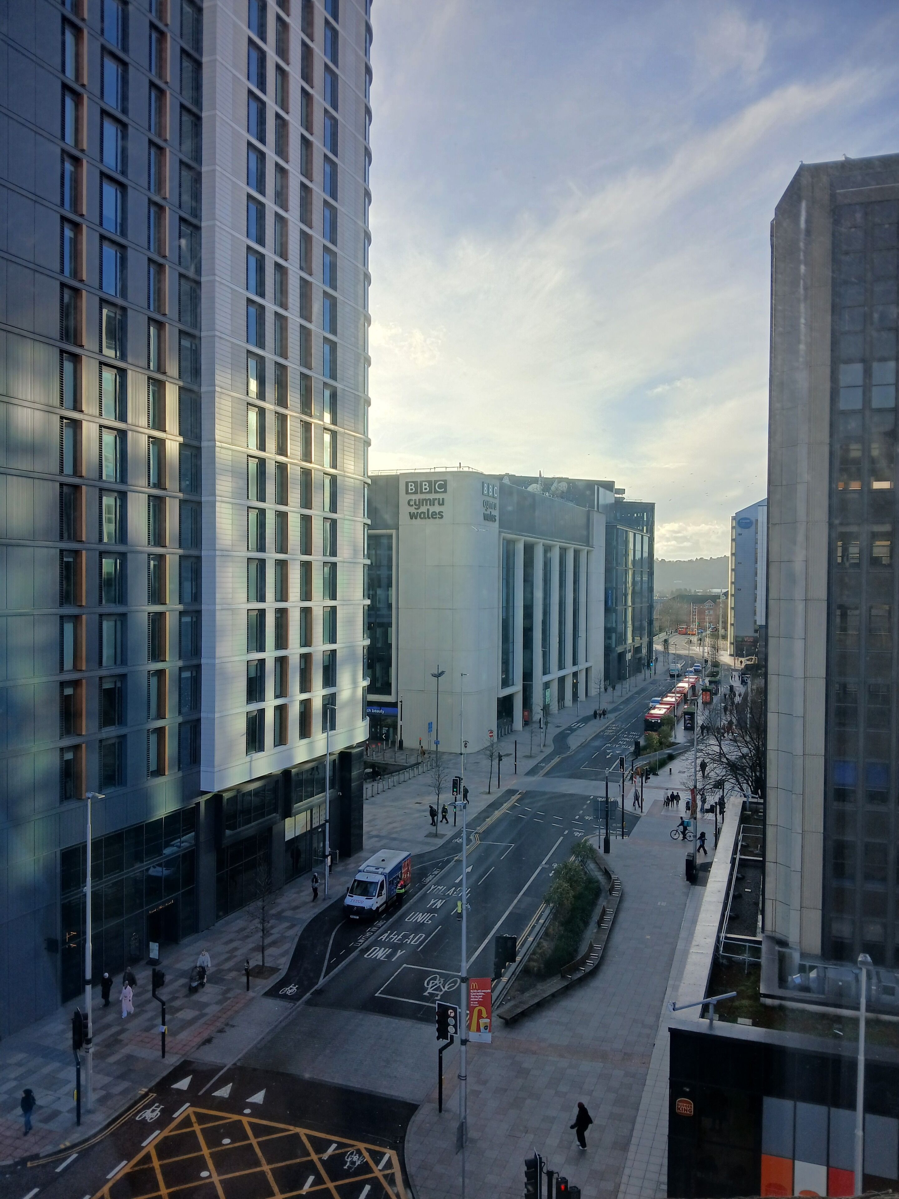 A modern urban street with high-rise buildings, a pedestrian crossing, and a McDonald's sign.