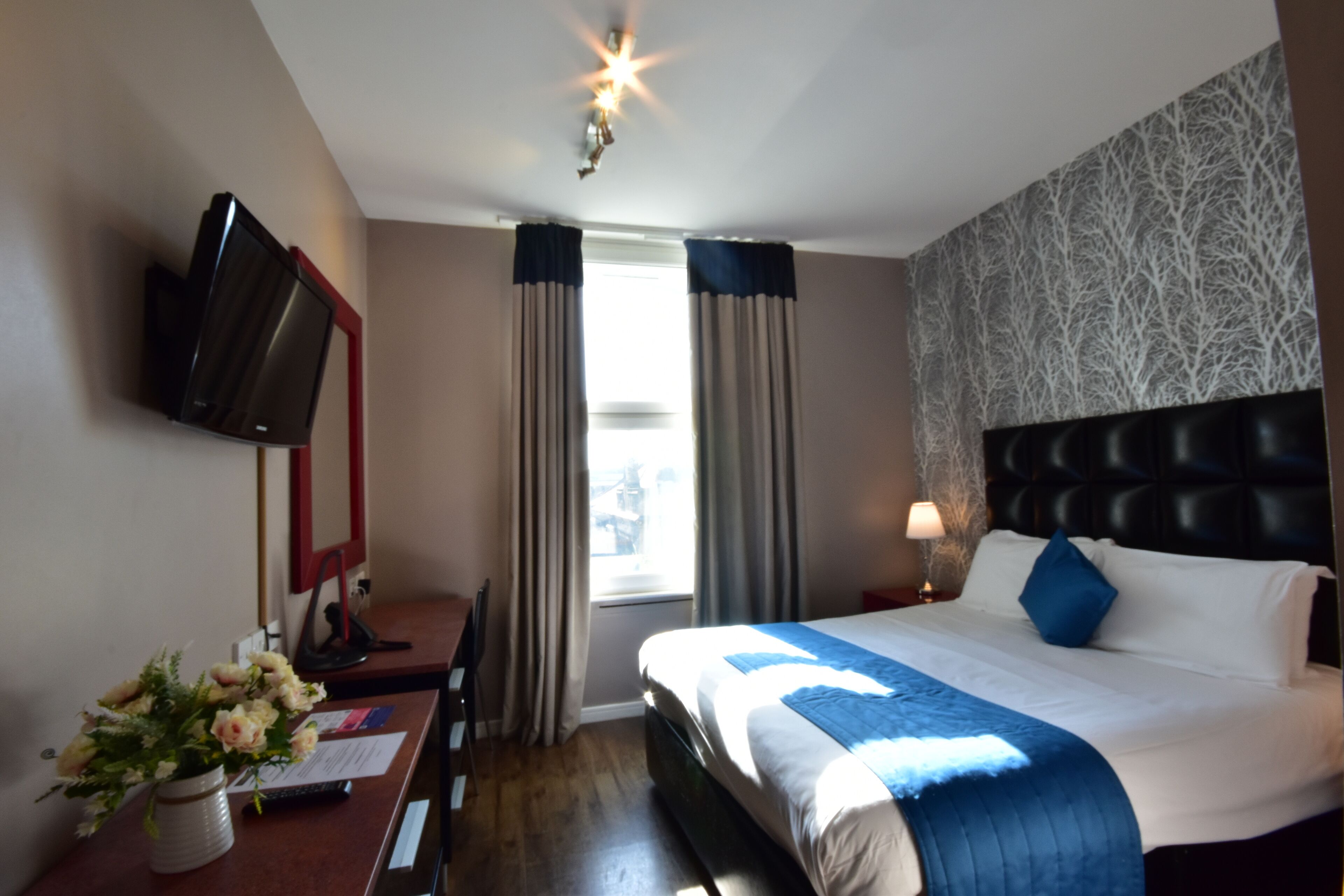 A hotel room with a bed, a desk with a computer, a TV, and a window with curtains.