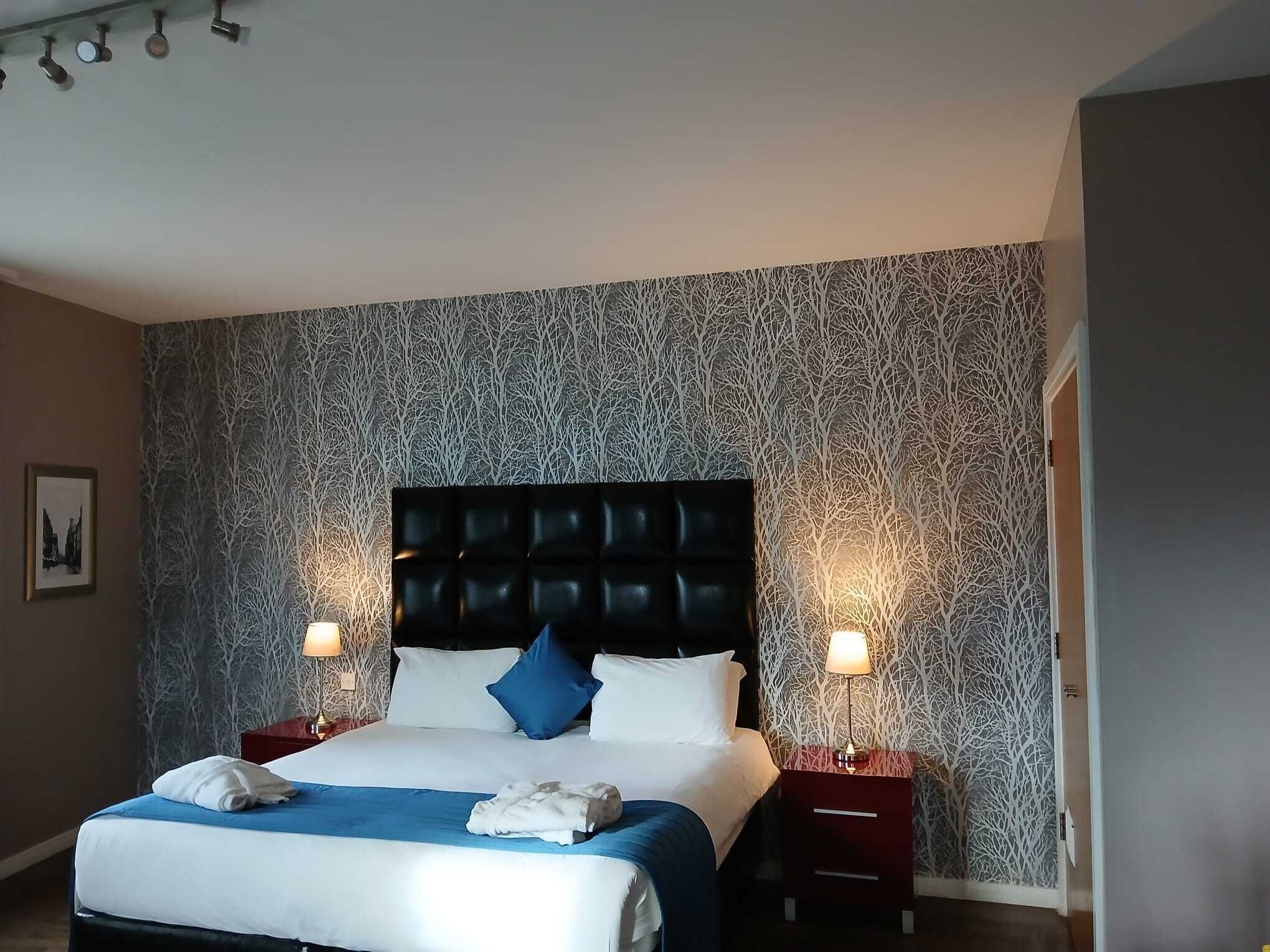 Quarto de hotel com uma cama grande, duas mesas de cabeceira e parede com padrão.