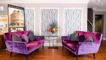 A reception area with two purple velvet sofas, a glass coffee table, and a decorative floral arrangement.