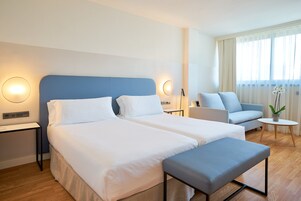 Habitación de hotel con dos camas, un sofá, una mesita y una planta en maceta.