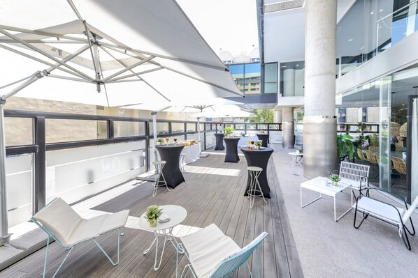 Terraza en la azotea con mobiliario exterior, sombrillas y plantas en macetas.