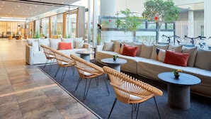 Un área de lounge moderna con diferentes disposiciones de asientos, incluyendo sofás y sillones, y vistas al exterior a través de amplias ventanas.