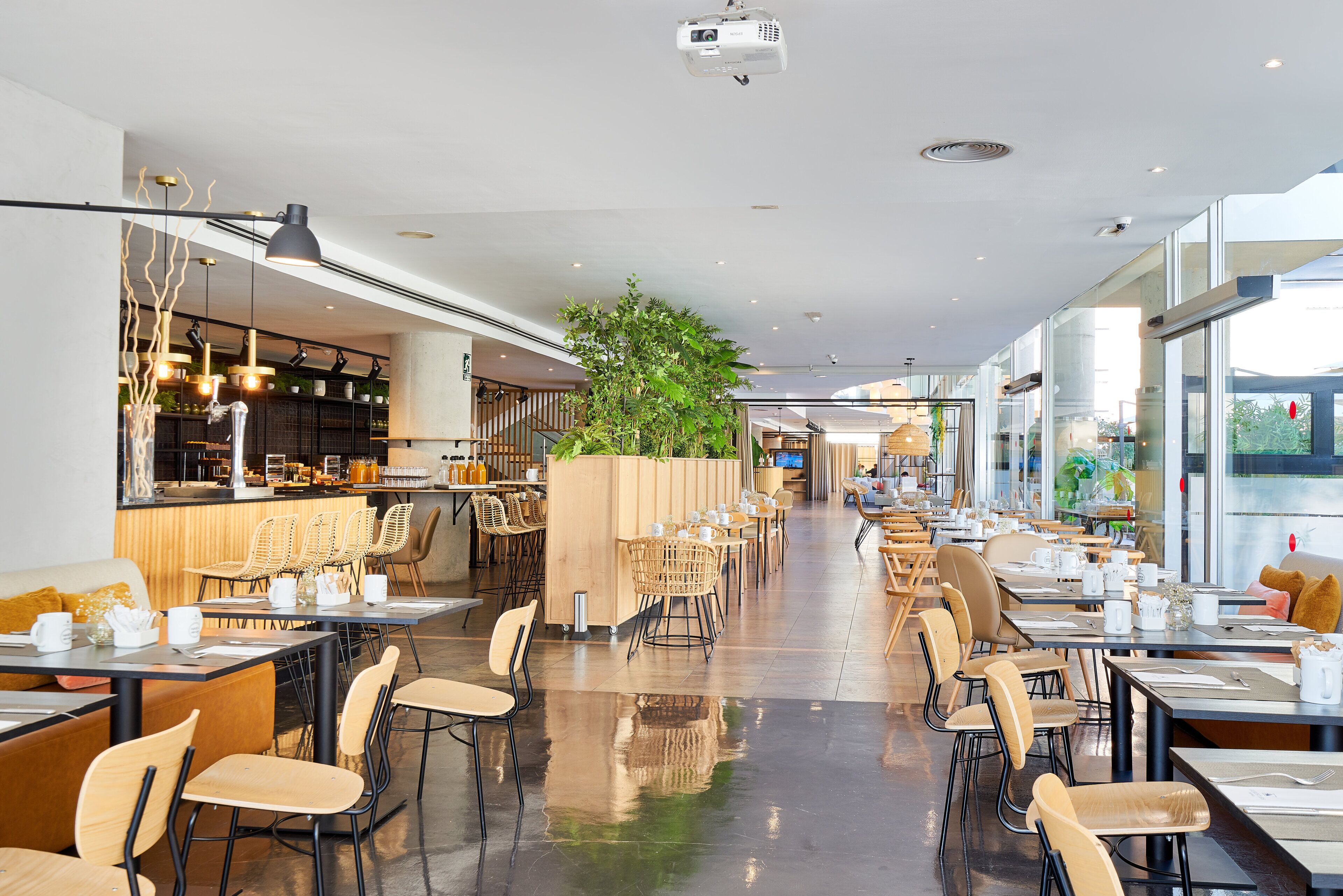 A modern restaurant with a long counter, multiple seating areas, and a central plant feature.
