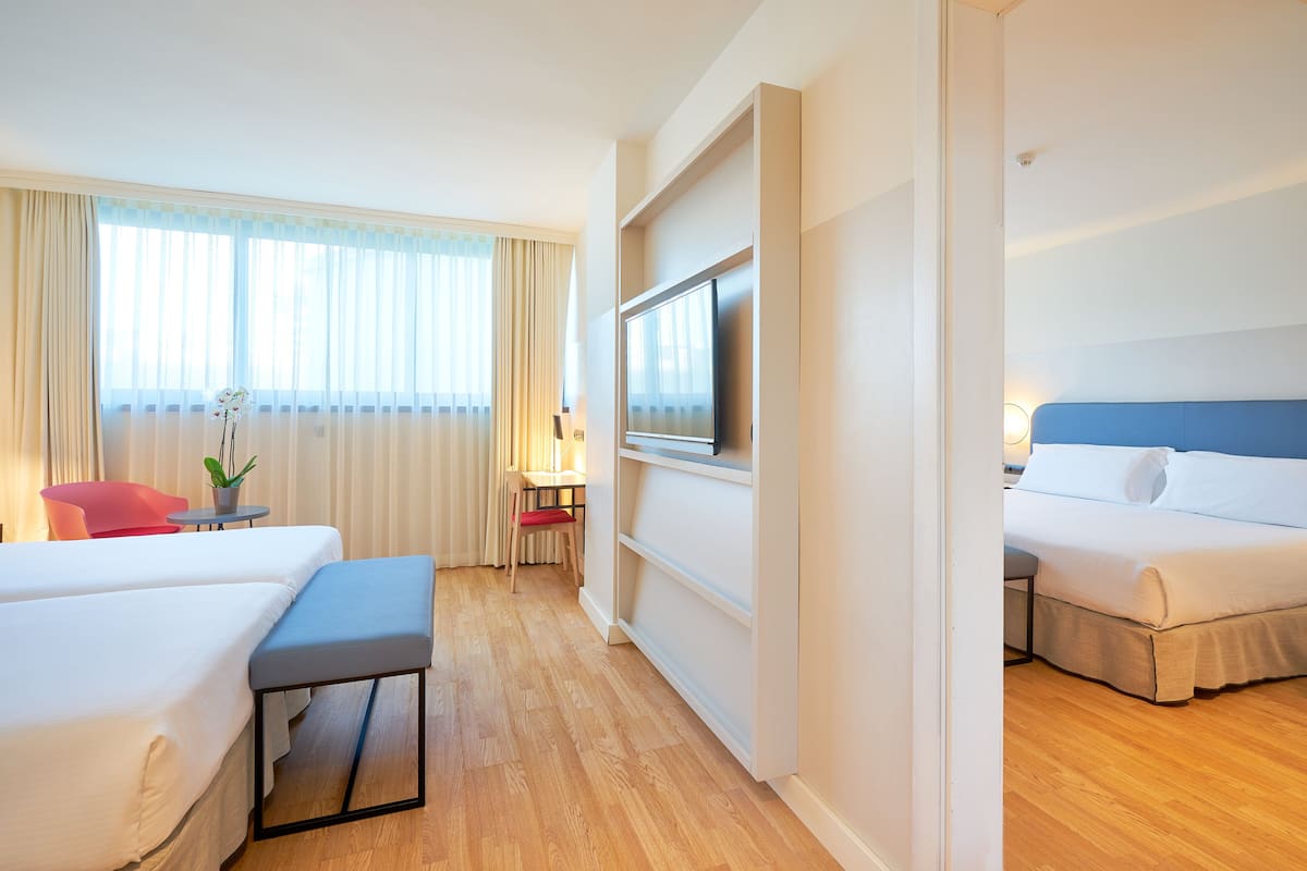 Habitación de hotel con dos camas, televisión, escritorio con silla y ventana con cortinas.