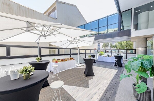 Eine Terrassenfläche im Freien mit Tischen, Stühlen und Sonnenschirmen, umgeben von modernen Gebäuden.