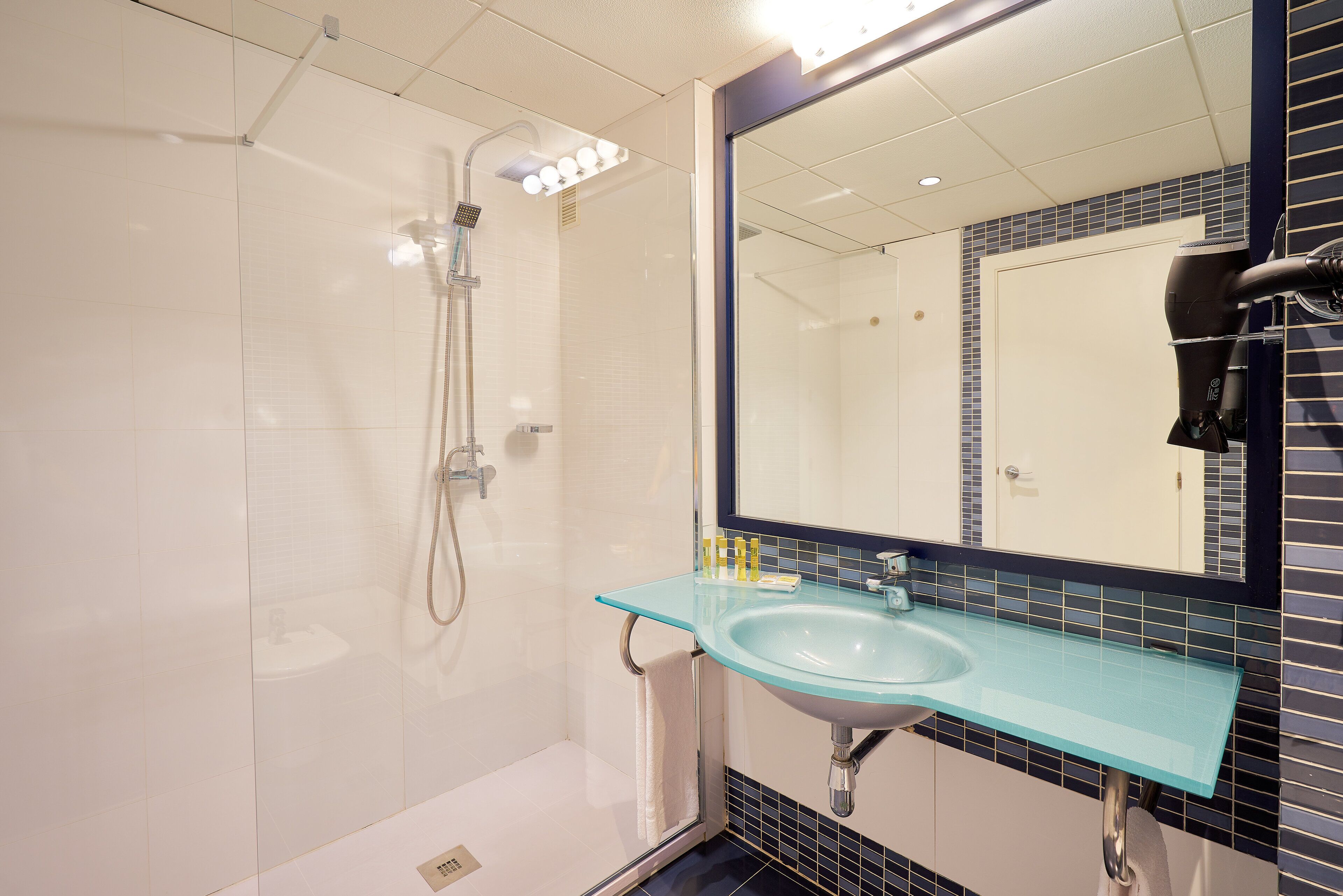 Un baño con cabina de ducha de vidrio, un lavabo con encimera azul y un espejo con marco negro.