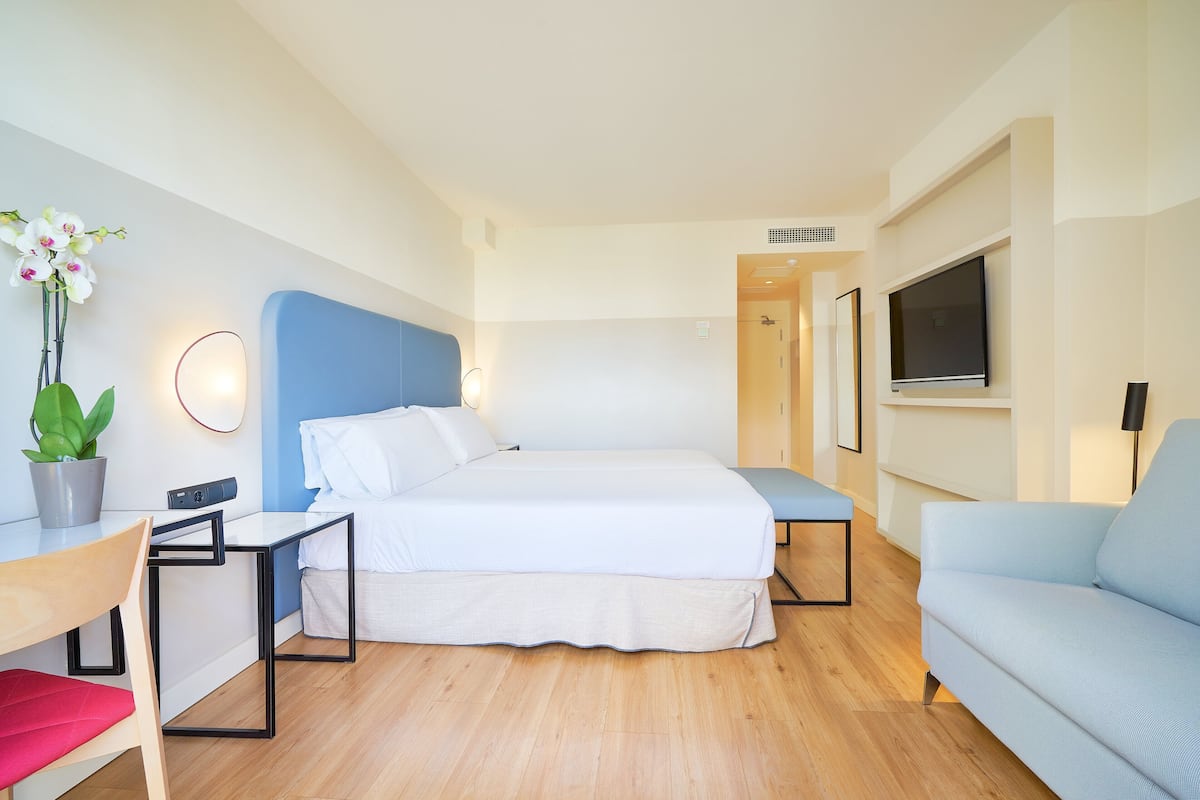Una habitación de hotel moderna con cama, escritorio, silla, sofá, televisor y planta en maceta.