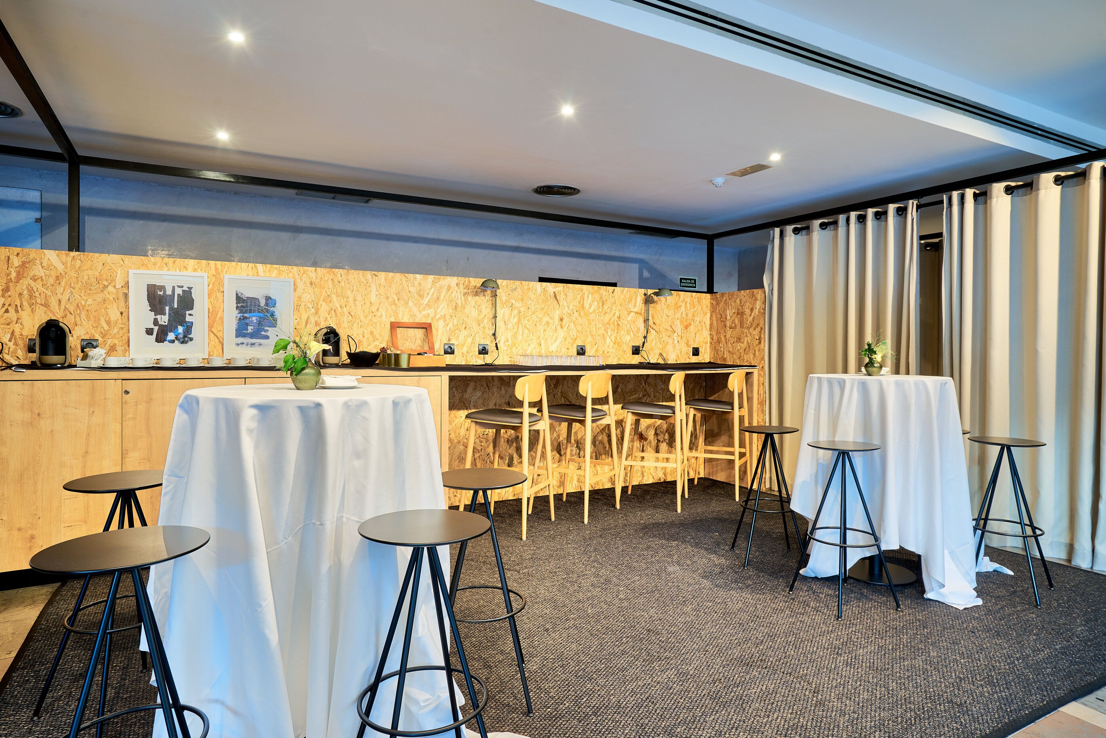 A hotel room with a wooden accent wall, a bar area, and a seating arrangement with tables and chairs.