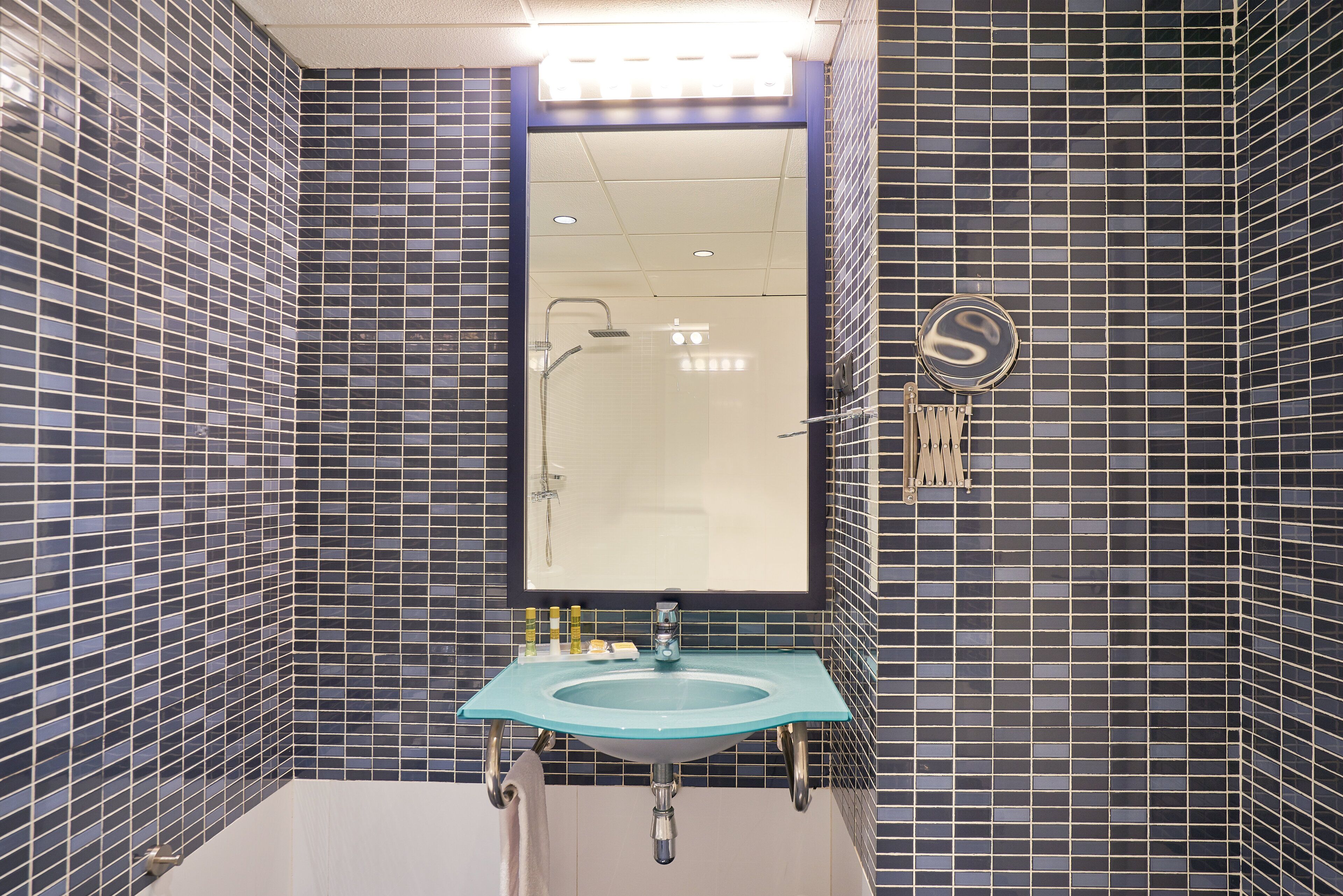 A bathroom with a large mirror, a sink, and a shower.