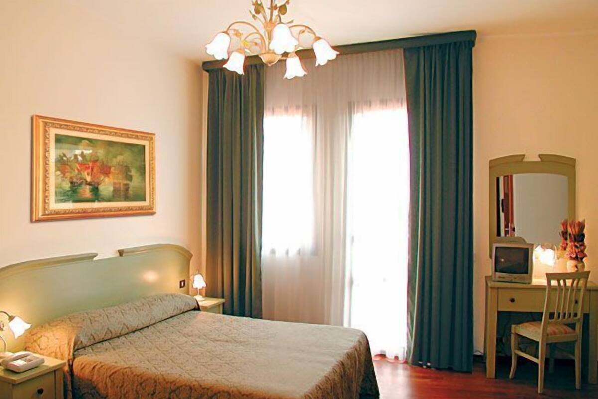 A hotel room with a bed, a desk, a chair, a television, and a painting on the wall.