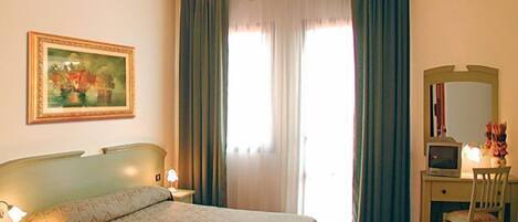 A hotel room with a bed, a desk, a chair, a television, and a painting on the wall.