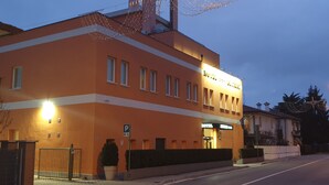 Um hotel com fachada laranja moderna, uma placa de estacionamento e uma entrada bem iluminada.