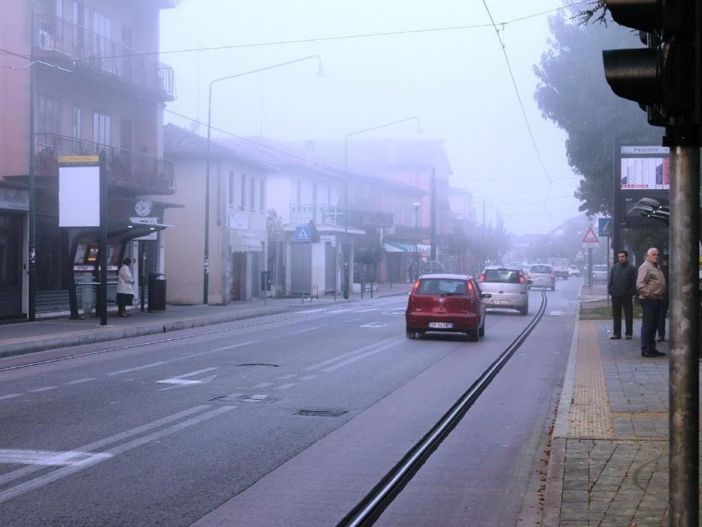 Vista da rua com linha de bonde, edifícios e alguns carros.