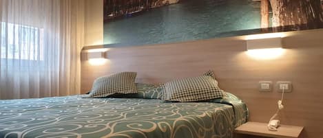 Una habitación de hotel con una cama, una mesita de noche, un teléfono y una lámpara fijada a la pared.