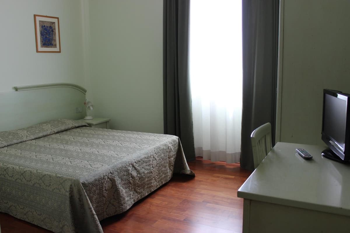 A room with a bed, a desk, a television, and a window with curtains.