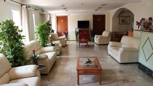 Uma sala de estar com sofás bege, uma mesa de centro e plantas em vasos.