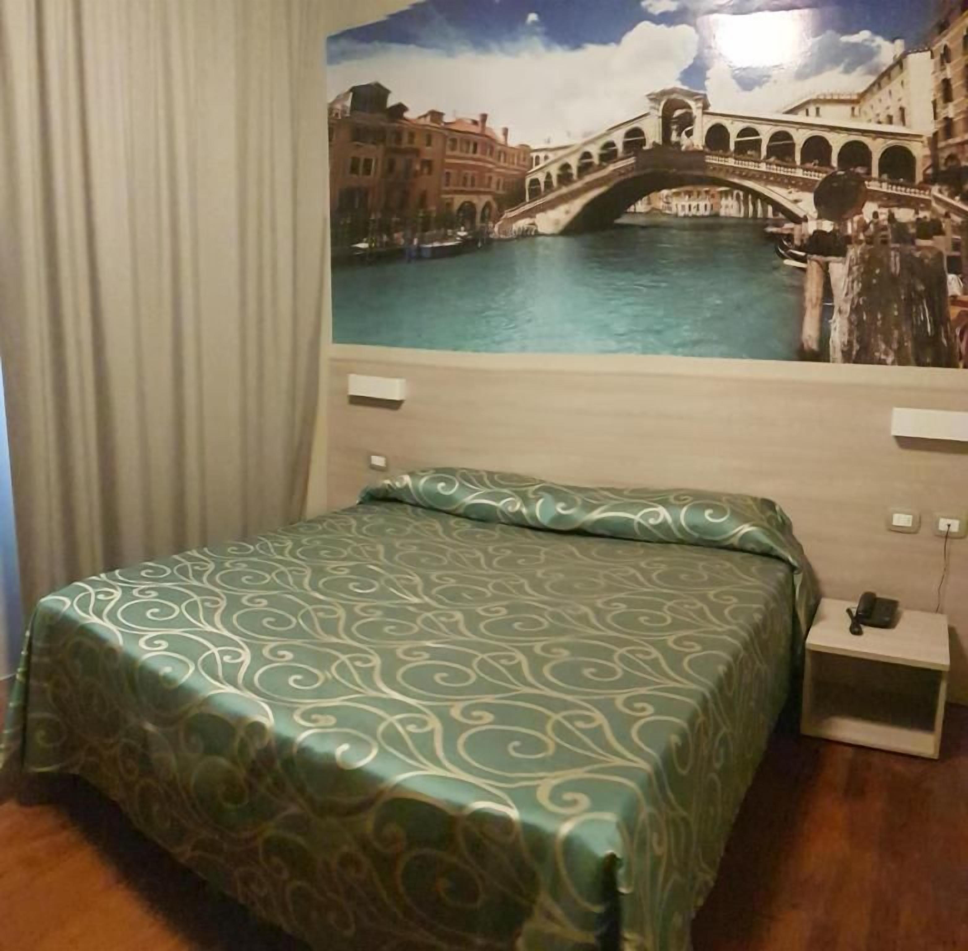 A hotel room with a bed, a nightstand, a telephone, and a wall mural of a cityscape.