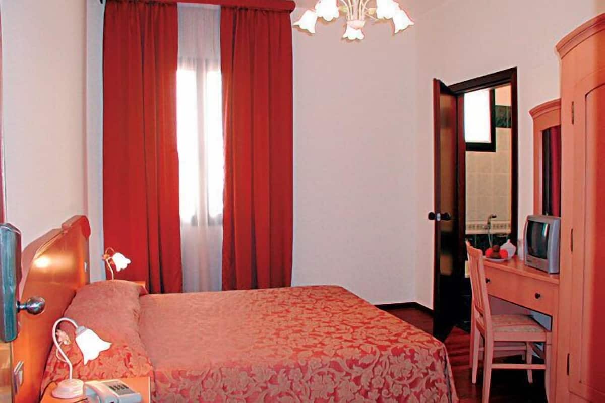 A hotel room with a bed, a desk with a television, a mirror, and a door leading to another room.