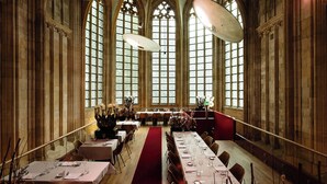 Un gran espai per a banquetes amb sostres alts, finestres allargades i un passadís central. Taules preparades per dinar amb cadires a banda i banda.
