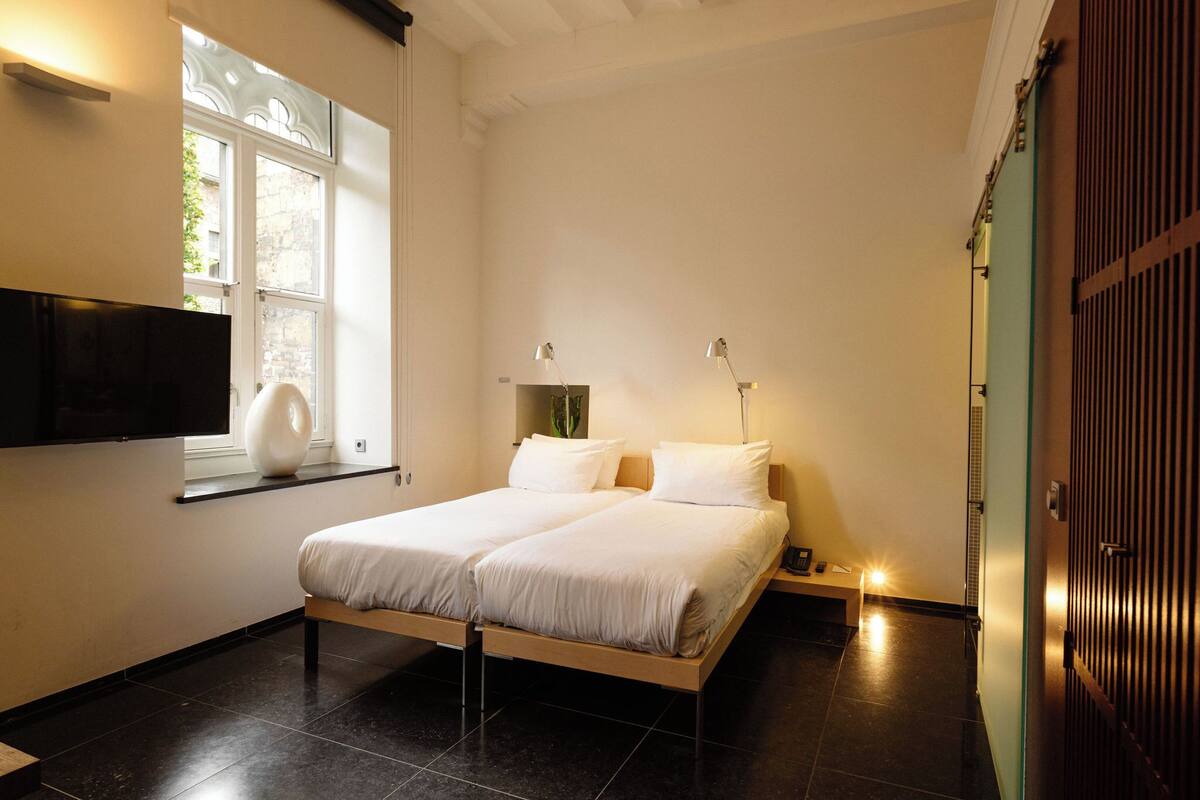 Un dormitorio con cama, televisor montado en la pared, ventana y puerta.